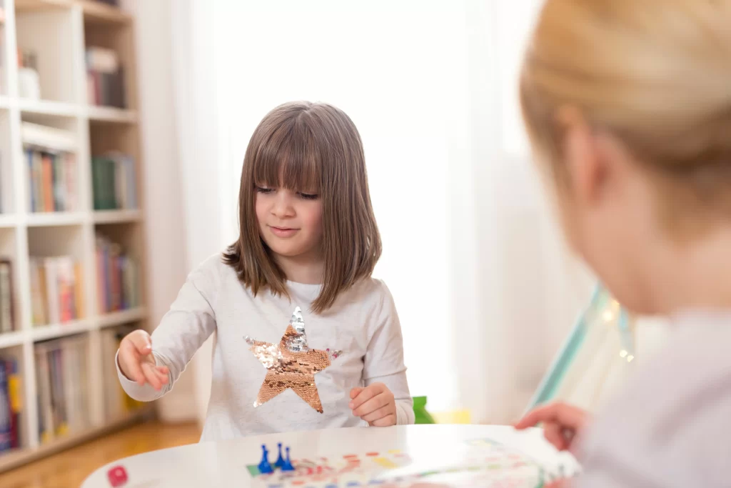 Una niña participa en un juego de mesa con un adulto, lo que podría ser una actividad utilizada en psicologia infantil para observar patrones de comportamiento.